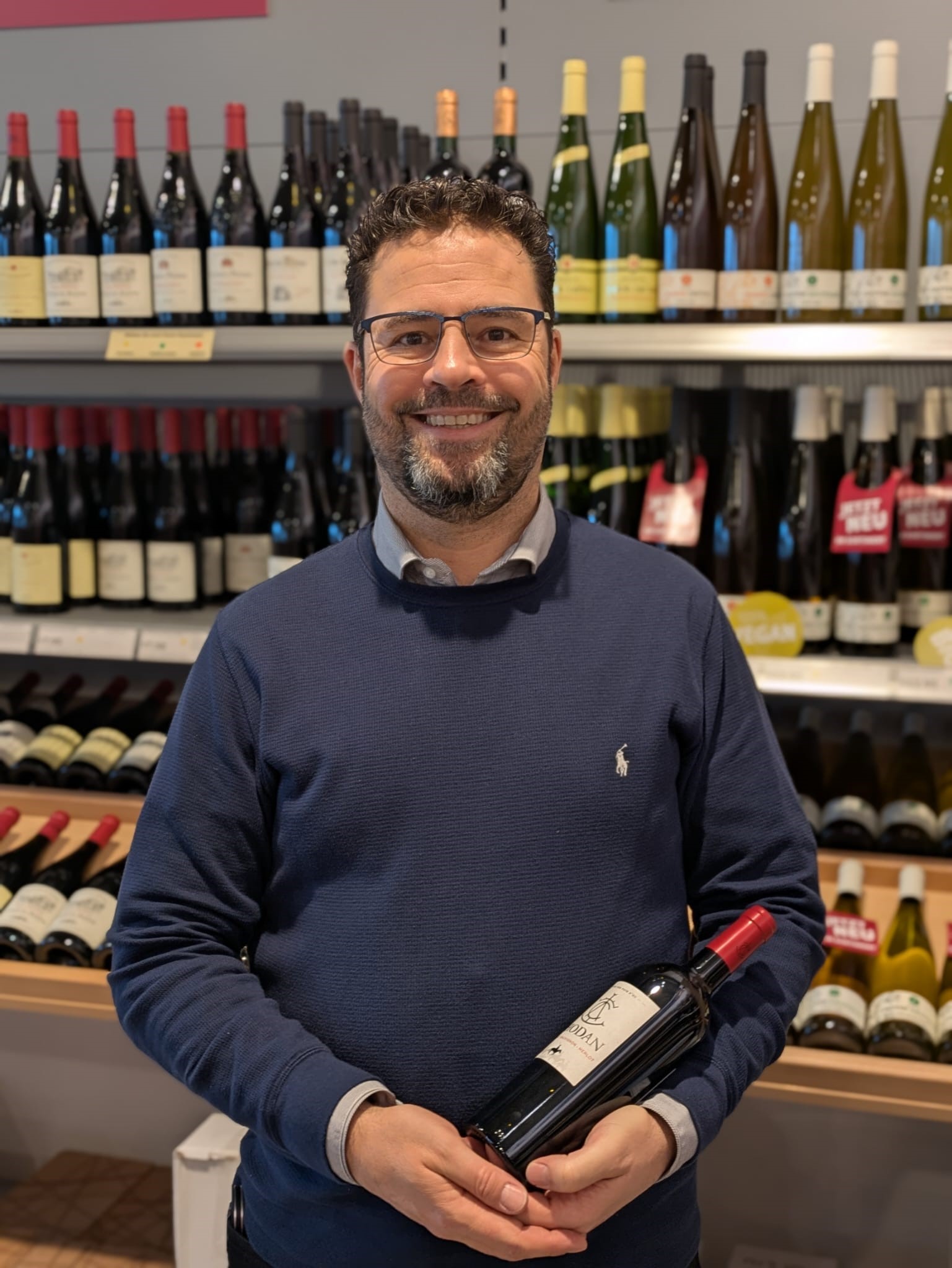 Mann hält Wein vor Weinflaschen, Weinshop.